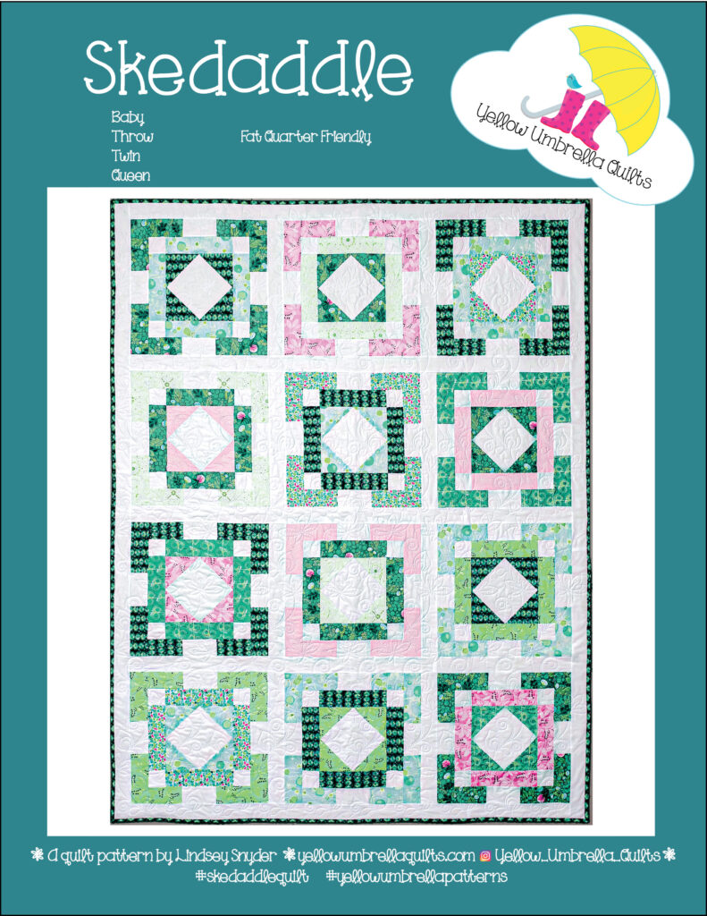 A quilt with green squares and red and pink pastels details made by Yellow Umbrella Quilts.